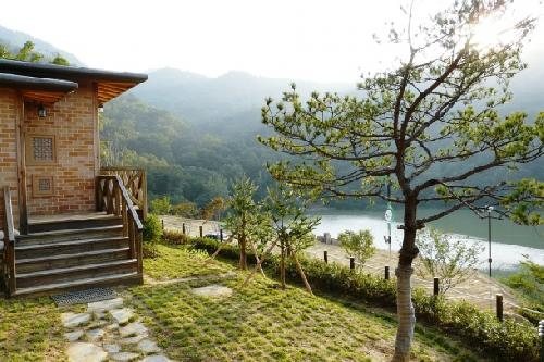 벽돌 숲속의 집 나무 계단 앞 잔디 마당과 소나무, 그 너머 산과 저수지