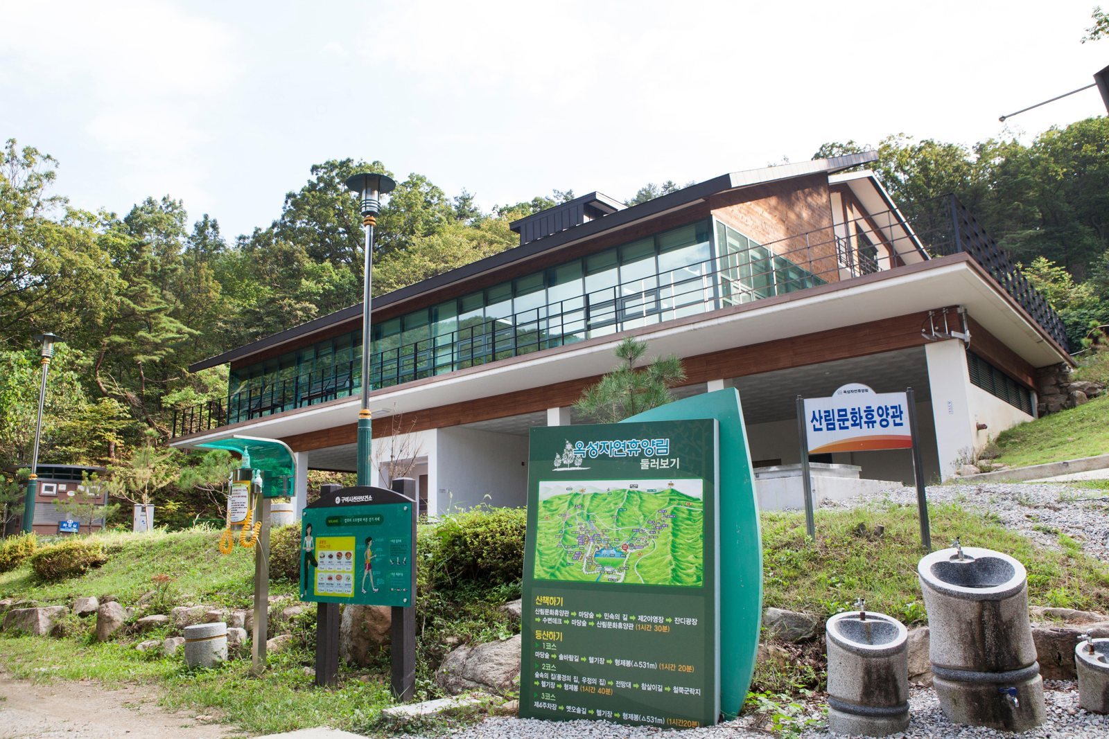 유리 벽 2층 건물 앞 ‘옥성자연휴양림 둘러보기’ 안내판과 ‘산림문화휴양관’ 간판